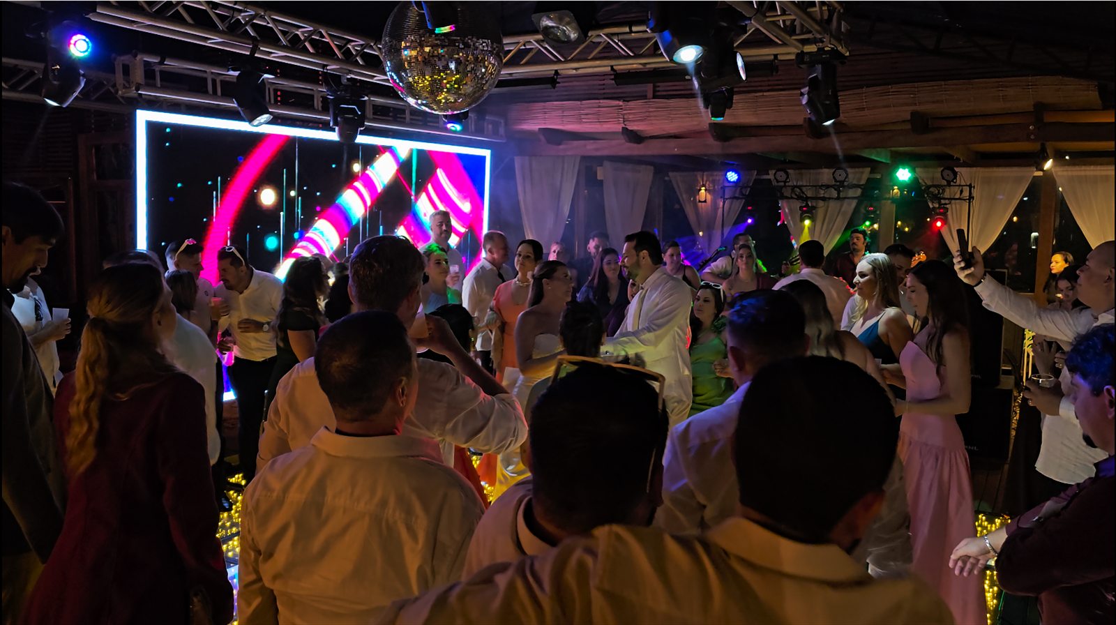 Convidados dançando em pista iluminada com painel de LED em casamento